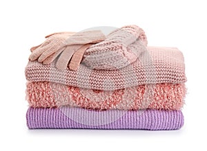 Stack of stylish sweaters, gloves and hat on white background