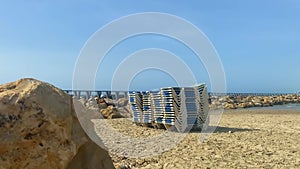 Stack of sun loungers on the sandy beach on the background of a not very stormy sea and the waves of which break on the breakwater