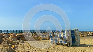 Stack of sun loungers on the sandy beach on the background of a not very stormy sea and the waves of which break on the breakwater