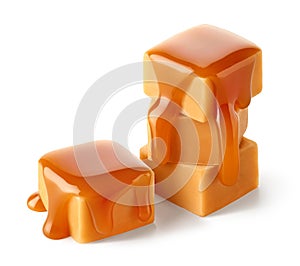 Stack of sweet caramel candy cubes topped with caramel sauce on white background