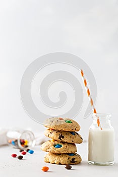 Stack of sweet cookies with colorful candies for children and a bottle of milk on white background. Side view, copy space. Bakery