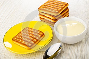 Stack of cookies, cookie in saucer, bowl with condensed milk, spoon on wooden table