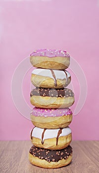 Stack of sweet glazed doughnuts on pink background.