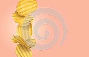 Stack of tasty ridged potato chips on pale coral background, space for text