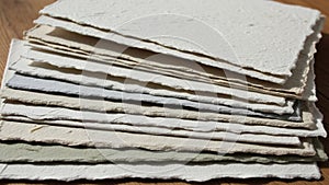 A stack of textured handmade paper sheets is arranged on a wooden surface
