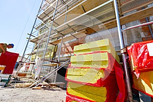 Stack of thermal insulation material is wrapped with cellophane foil. Unfinished edifice with scaffolding