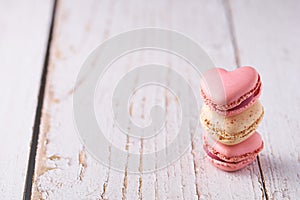 Stack of three heart shaped cream filled French macaroons on white wooden background. Confections for Valentine\'s Day