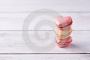 Stack of three heart shaped cream filled French macaroons on white wooden background. Confections for Valentine\'s Day