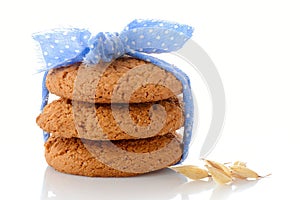 Stack of three homemade oatmeal cookies tied with blue ribbon in small white polka dots and ear of oats