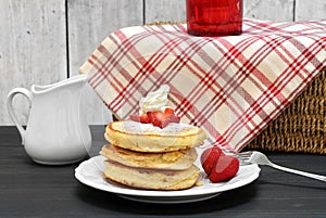 A stack of three pancakes garnished with fresh strawberry slices and whipped cream