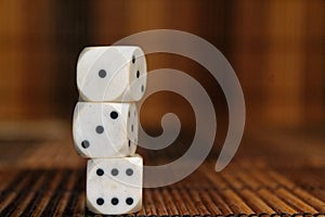 Stack of three white plastic dices on brown wooden board background. Six sides cube with black dots. Number 1, 3, 6