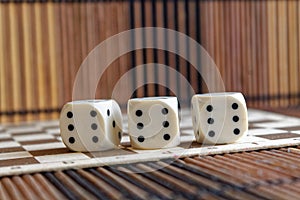 Stack of three white plastic dices on brown wooden board background. Six sides cube with black dots. Number 6