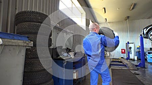 Stack of tires and male mechanic take one. Seasonal car tire changing in garage