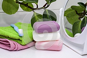 A stack of towels soap toothbrush mirror and houseplant on the bathroom table