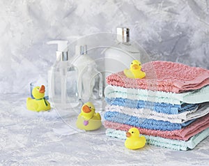 Stack of towels with yellow rubber bath ducks on white marble background, space for text, selective focus