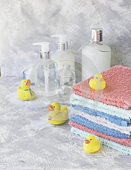 Stack of towels with yellow rubber bath ducks on white marble background, space for text, selective focus