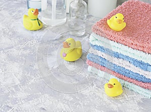 Stack of towels with yellow rubber bath ducks on white marble background, space for text, selective focus