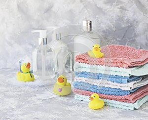 Stack of towels with yellow rubber bath ducks on white marble background, space for text, selective focus