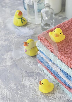 Stack of towels with yellow rubber bath ducks on white marble background, space for text, selective focus