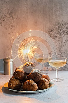 A stack of traditional oliebollen (Dutch dough fritters) with a glass of champagne on white background with sparklers