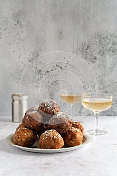 A stack of traditional oliebollen (translation: Dutch dough fritters) with a glass of champagne on white background