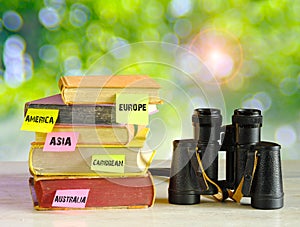 stack of travel Guides,travel books,guidebooks for various destinations and vintage binoculars on blurred nature background,free