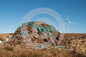 Stack of turf in a bog next to wind farm turbine. Clean new and dirty old source of energy. Natural and artificial product in
