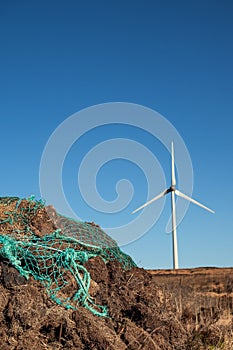 Stack of turf in a bog next to wind farm turbine. Clean new and dirty old source of energy. Natural and artificial product in