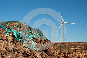 Stack of turf in a bog next to wind farm turbine. Clean new and dirty old source of energy. Natural and artificial product in