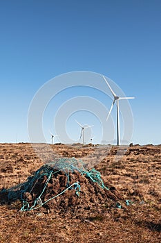 Stack of turf in a bog next to wind farm turbine. Clean new and dirty old source of energy. Natural and artificial product in