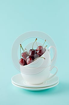 Stack of two white teacup with sweet cherry on cyan background.