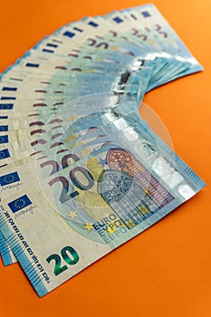 A stack of used blue 20 euro banknotes  on a vivid orange background.