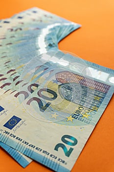 A stack of used blue 20 euro banknotes  on a vivid orange background.