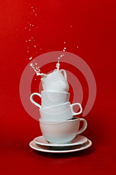 Stack of various cups and saucers with creamer on top and splash