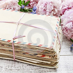 Stack of vintage love letters and pink peonies in the background