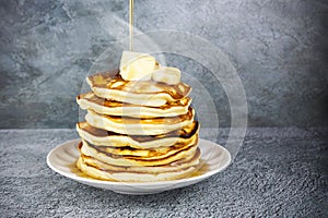 Stack of warm pancakes with steam on white plate with piece of butter, sliced banana and maple syrup on gray surface