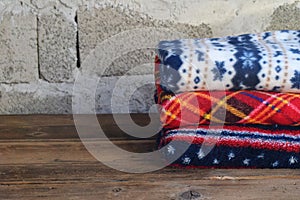 Stack of warm woolen blankets on wooden background. Home cosiness. Colorful plaids