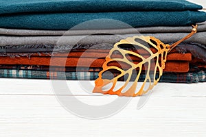 Stack of warm woolen scarf lying on wooden table and decorated autumn leaves