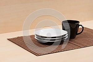 Stack of the white and black plates near black cup on tablemat.