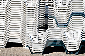 Stack of white and green  plastic  empty chairs on beach . Beginning or ending the summer season