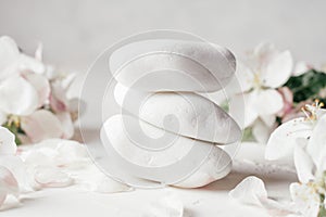 Stack of white pebble stones on light plaster surface, with apple flowers