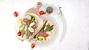 Stack whole grain tortillas. Ingredients for Flatbread Paratha roti cherry tomatoes, asparagus, on light gray background. Top view