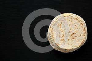 Stack of Whole Wheat Flour Tortillas on a black background, top view. Flat lay, overhead, from above. Copy space