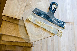 Stack of wood parquet or floorboard as floor covering with spatula on it with parquet adhesive glue on it top view. Preparation fo