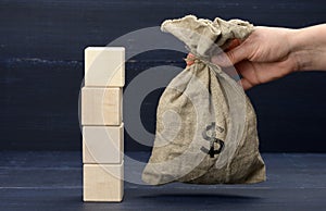 A stack of wooden cubes and a woman`s hand holds a full bag with a dollar sign. Savings concept, subsidy from the state