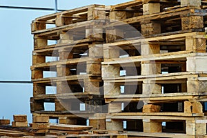 A stack of wooden pallets in an internal warehouse. An outdoor pallet storage area under the roof next to the store. Piles of Euro