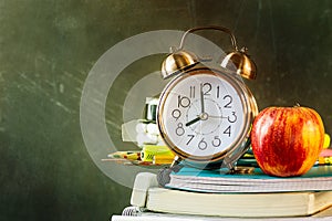 Stack of workbooks pens pencils alarm clock red apple on vintage scratched chalkboard background. Back to school education