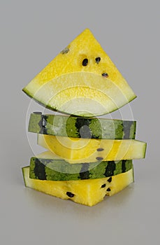 a stack of yellow watermelon slices on a gray background, with a triangular piece on top.