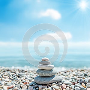 Stack of zen stones near sea and clouds with sun