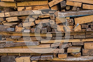 Stacked as a woodpile are many wooden yellow gray boards, planks, and slats of various sizes